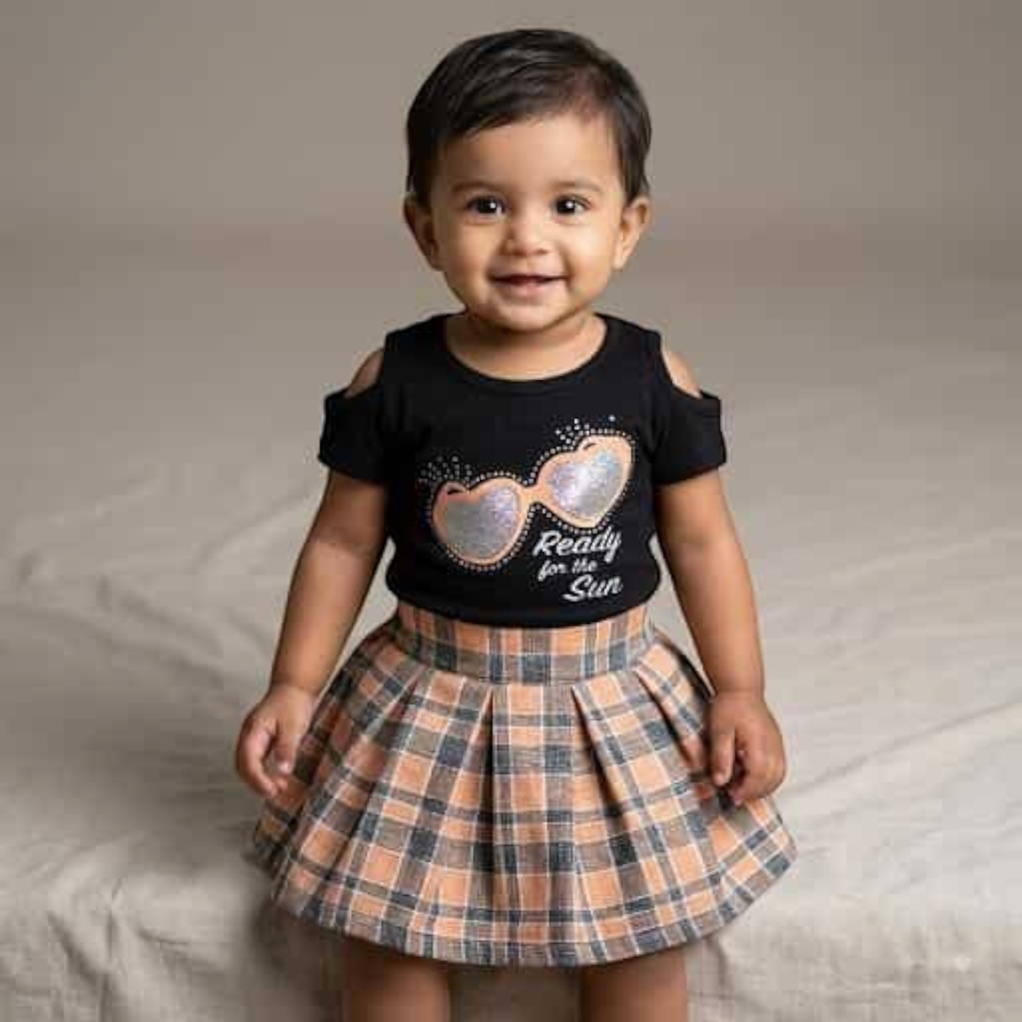 City Center toddler girl wearing a black cold-shoulder top and a pleated plaid skirt with orange and grey tones