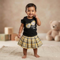 City Center toddler girl wearing a yellow plaid pleated skirt and a black graphic t-shirt in a studio setting