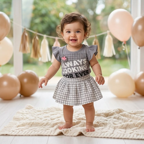 City Center baby girl wearing a grey windowpane check top and matching flared skirt in a festive balloon-filled room