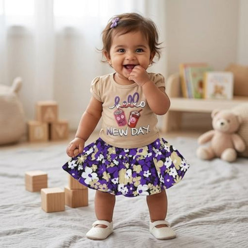 City Center baby girl wearing a beige graphic t-shirt and a purple floral flared skirt in a bright nursery setting.