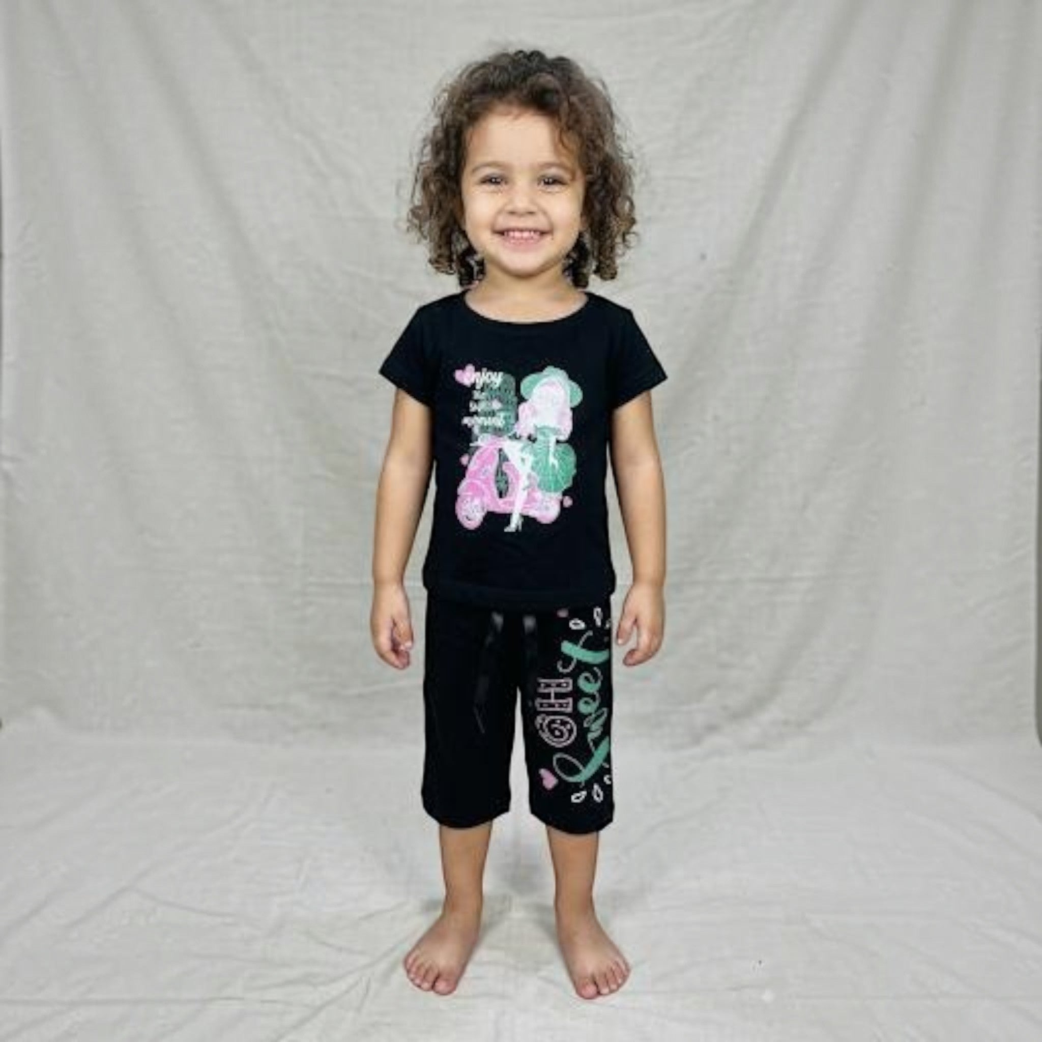 A young girl smiling while wearing a City Center black co-ord set with a graphic print top and matching shorts.