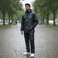 A man wearing a black City Center waterproof raincoat and matching trousers standing on a wet cobblestone path.