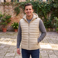 City Center man wearing a beige Calvin Klein hooded puffer vest over a grey long-sleeve shirt in a garden setting