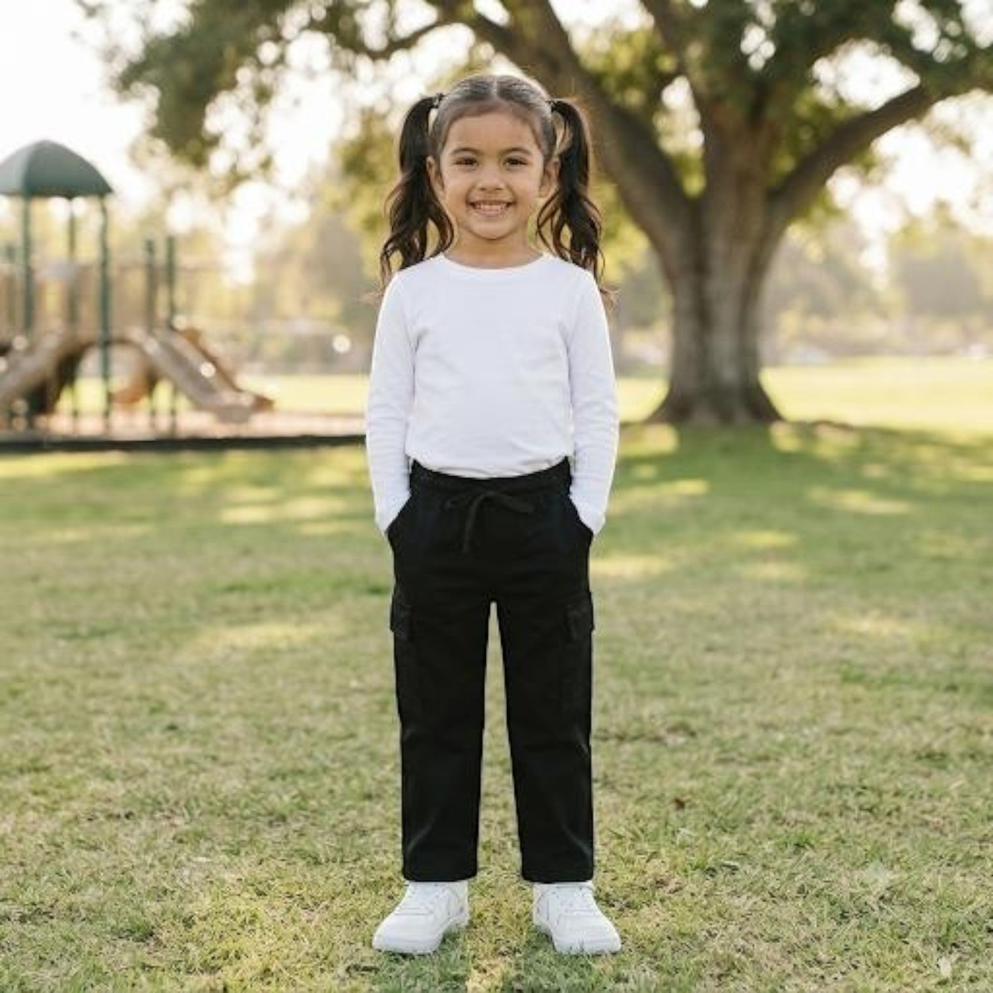 City Center girls black ethnic cargo pants with elasticated waist worn with a white long sleeve top in a park