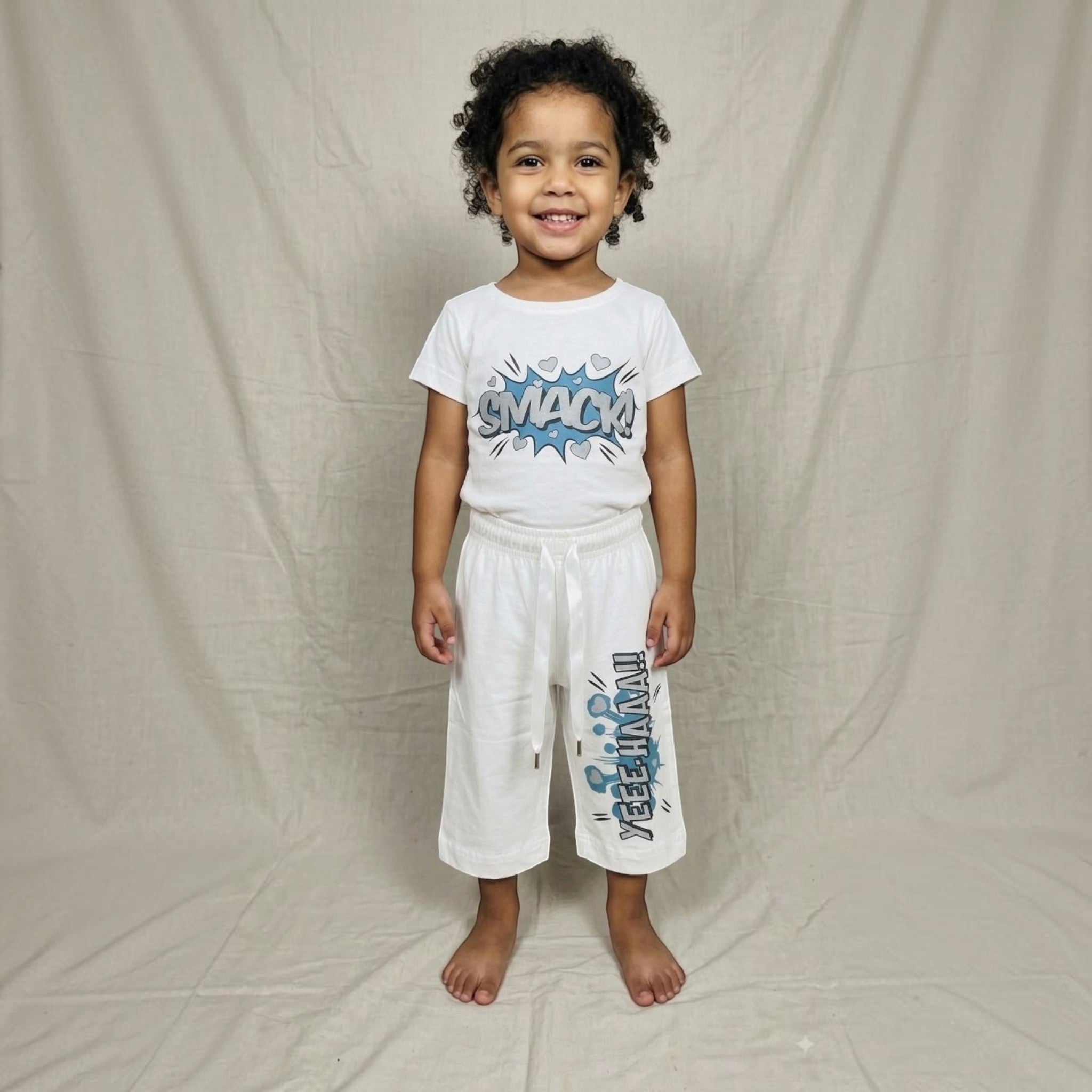 City Center kids white co-ord set with comic book style SMACK and YEEHAA print worn by a smiling young girl