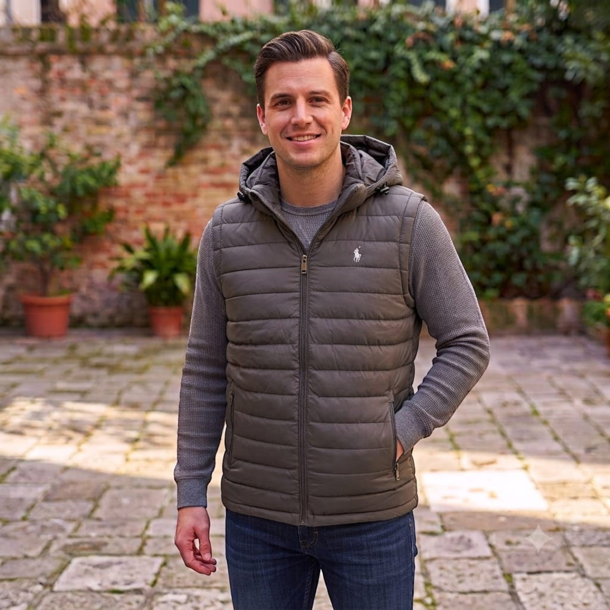 City Center olive green quilted hooded vest worn by a man over a grey sweater in an outdoor courtyard setting