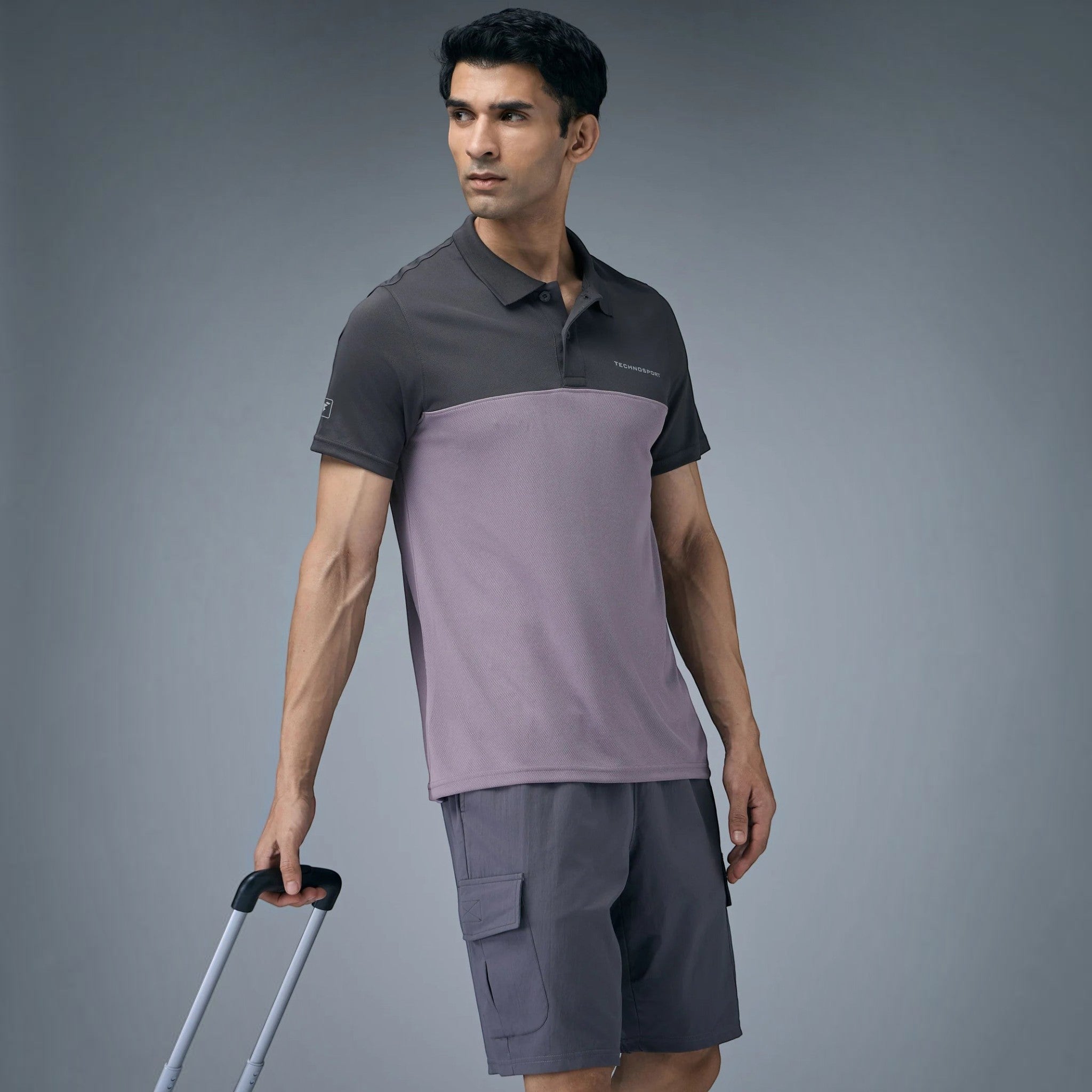 City Center model wearing a two-tone grey performance polo shirt and matching cargo shorts while holding luggage