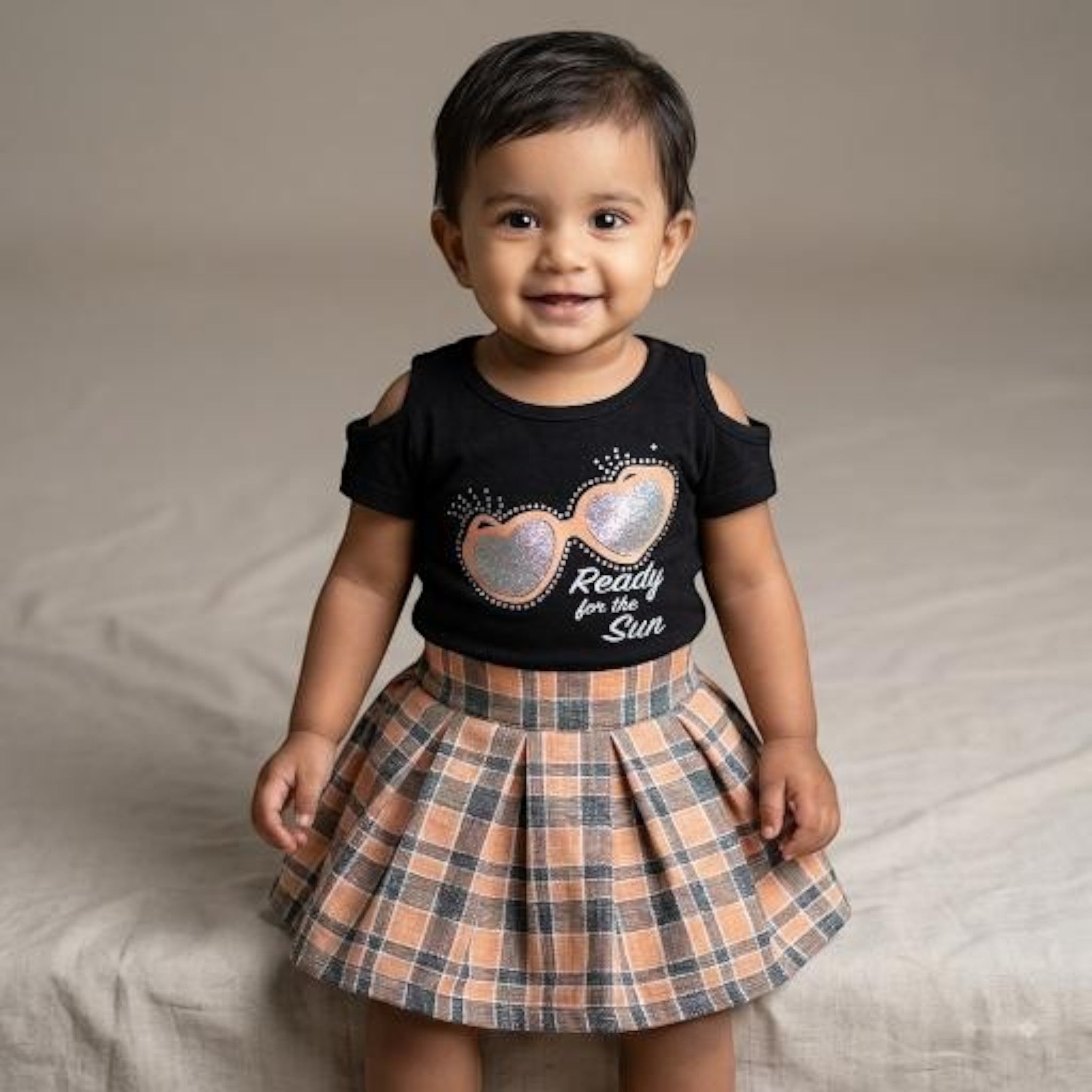 City Center toddler girl wearing a pleated plaid skirt and black cold-shoulder top with sunglasses graphic