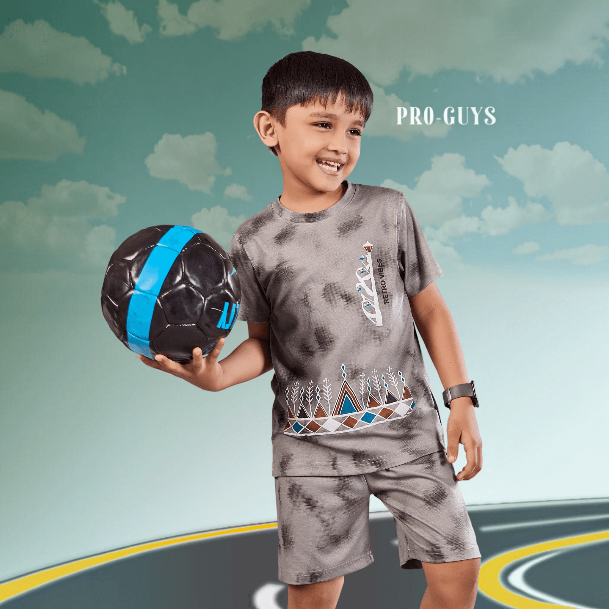City Center Pro-Guys kids grey tie-dye cotton t-shirt and shorts set worn by a smiling boy holding a soccer ball