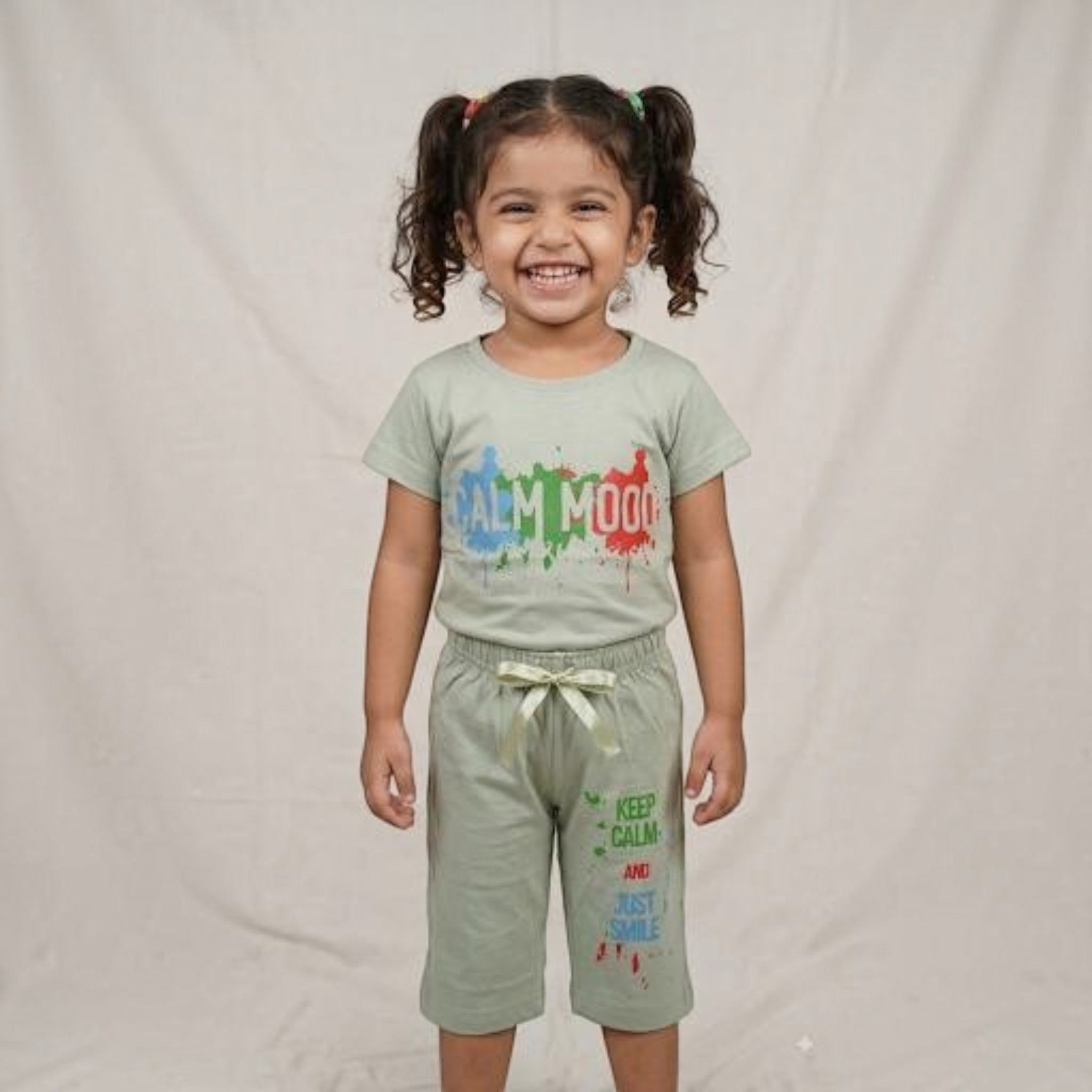 A young girl smiling while wearing a sage green City Center co-ord set with colourful graphic text prints.