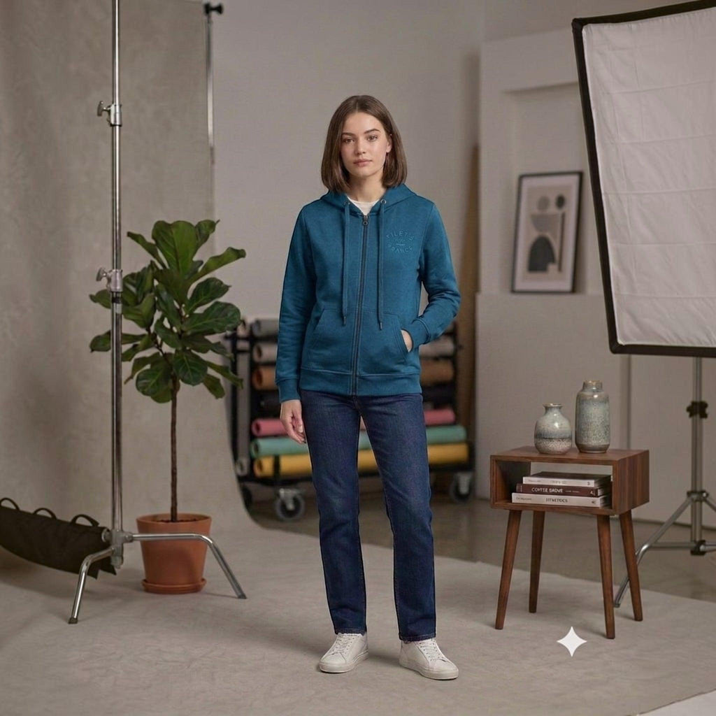 City Center teal full zip hooded sweatshirt worn by a woman with dark jeans and white sneakers in a studio setting