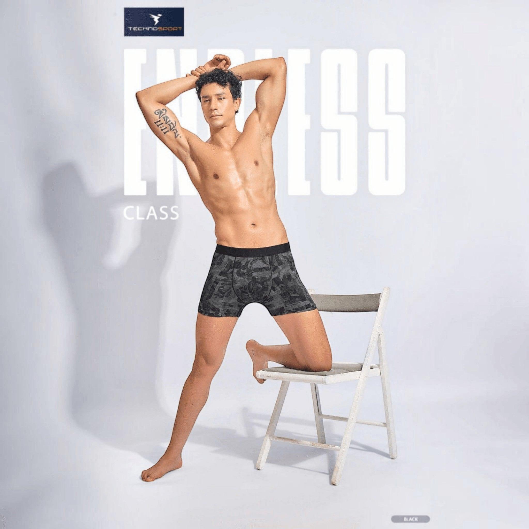 City Center Technosport men's black patterned trunk with soft-touch elastic waistband worn by a model on a chair.