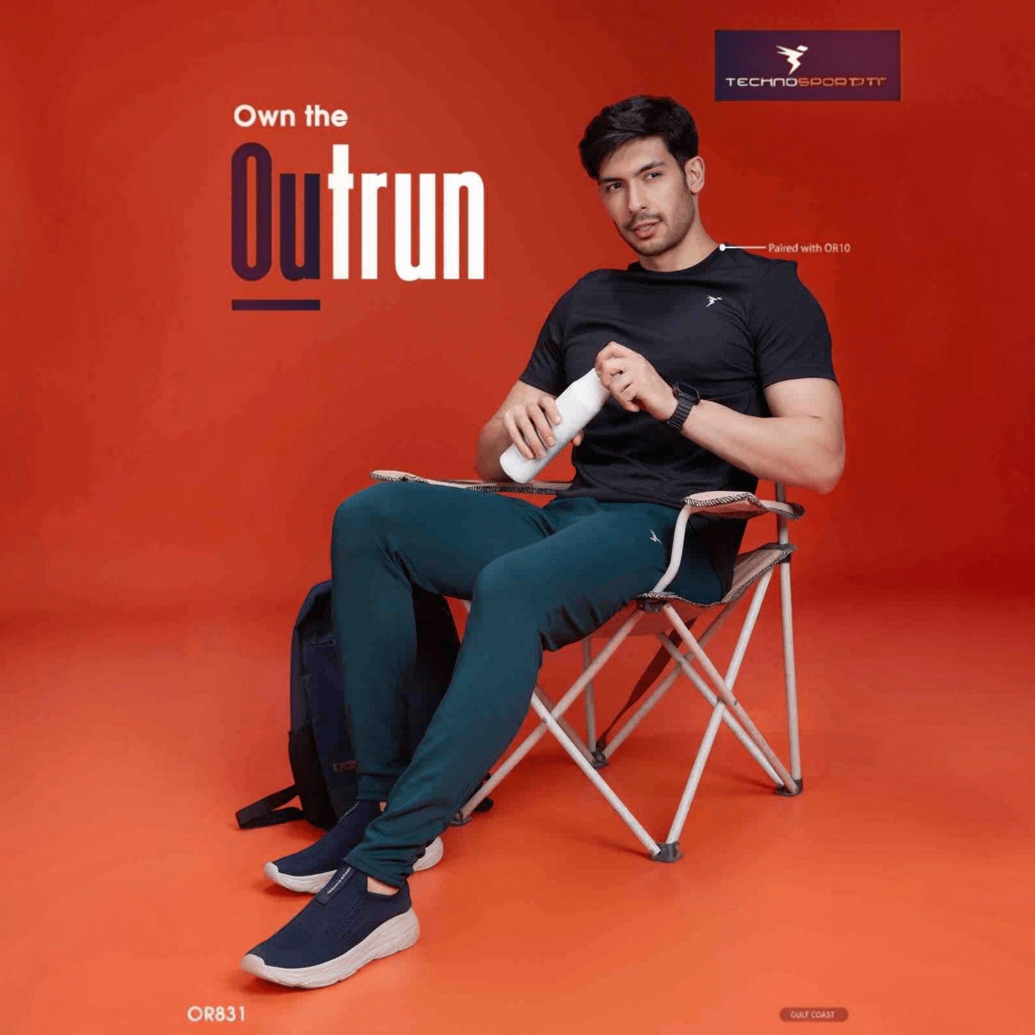 City Center Technosport men's slim-fit performance track pants in dark teal, worn by a model sitting on a chair.