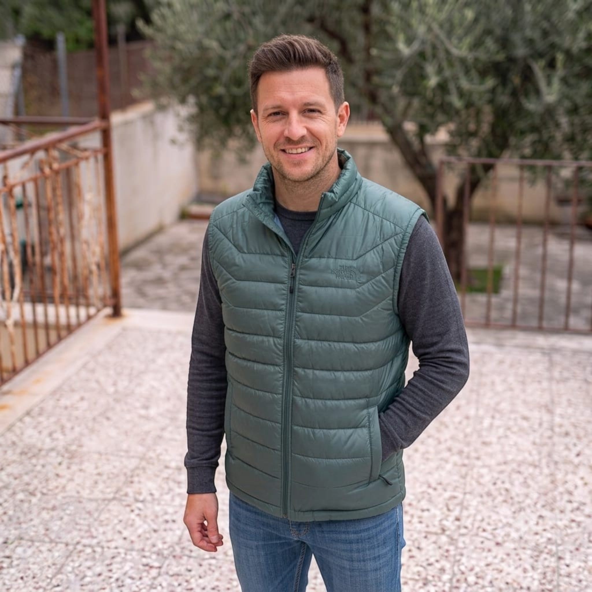 City Center model wearing a sage green The North Face insulated puffer vest over a grey sweater outdoors