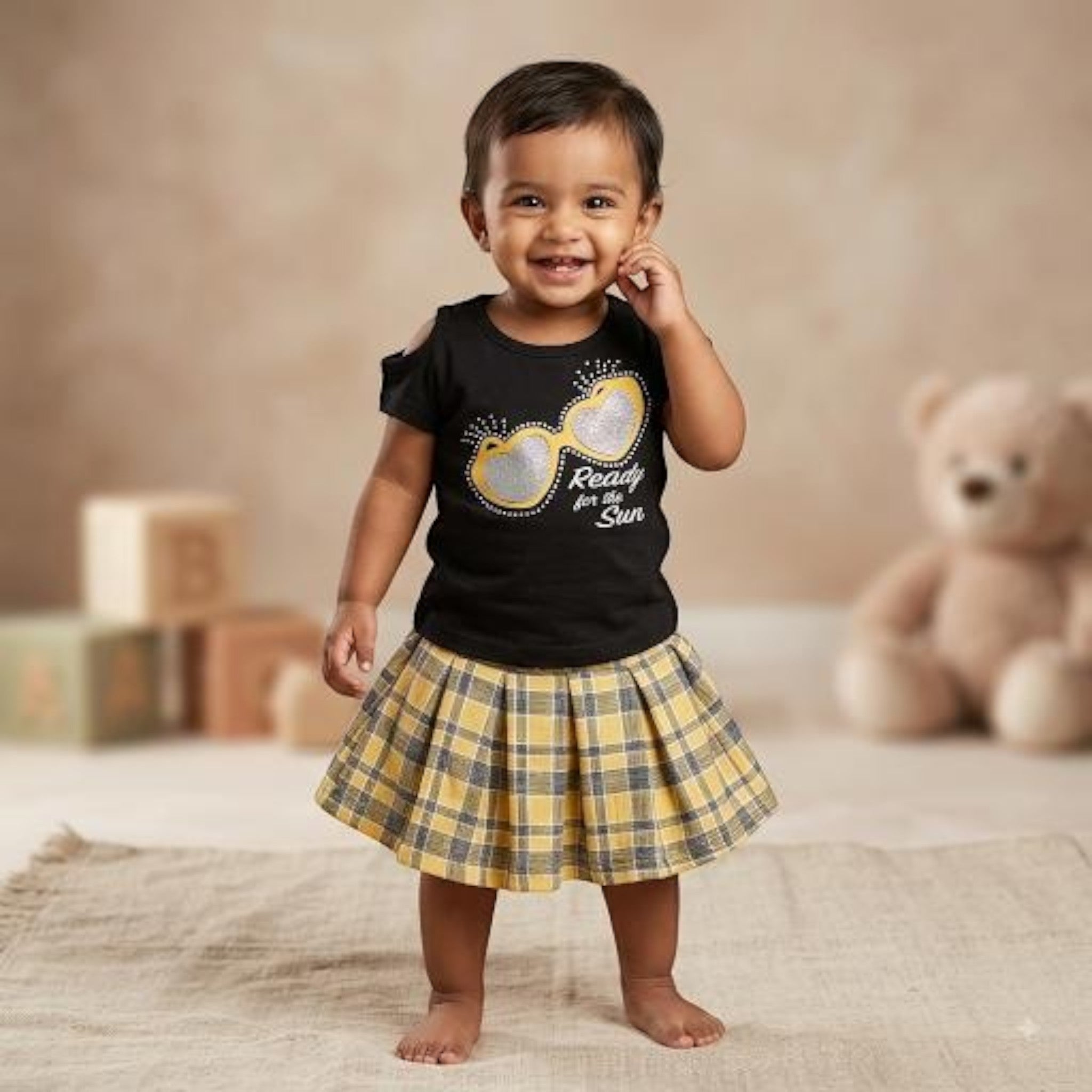 City Center toddler girl wearing a black cold-shoulder top and a yellow and grey plaid flared skirt in a studio.