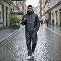 City Center Fine Touch waterproof raincoat in black worn by a man holding an umbrella on a rainy city street.