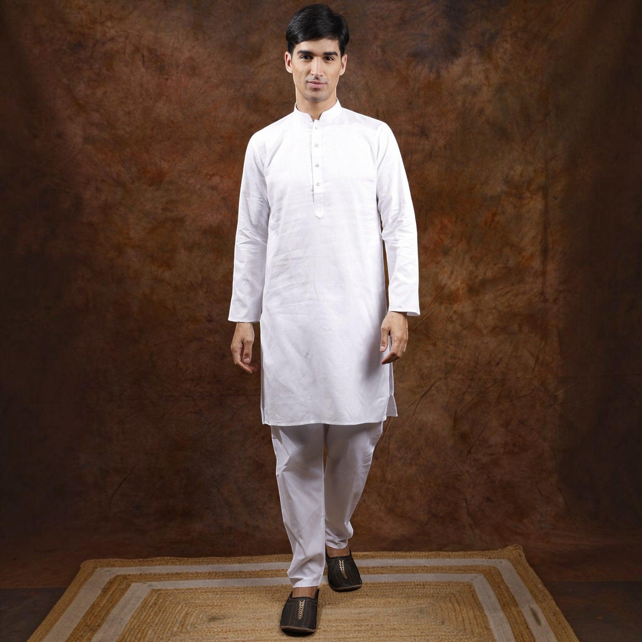A man wearing a City Center white cotton kurta pyjama set, standing on a jute rug against a rustic brown backdrop.