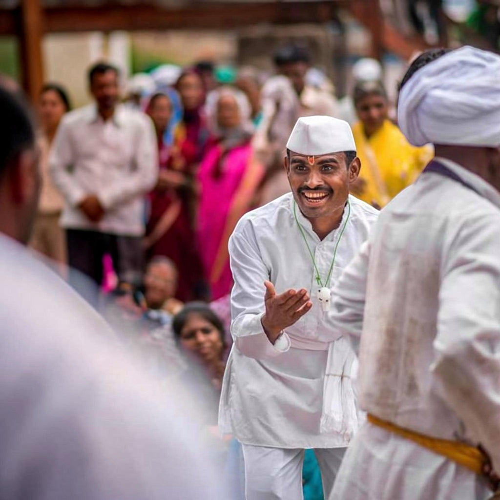 Man wearing a City Center white cotton kurta and traditional cap, dancing during a festive cultural celebration.
