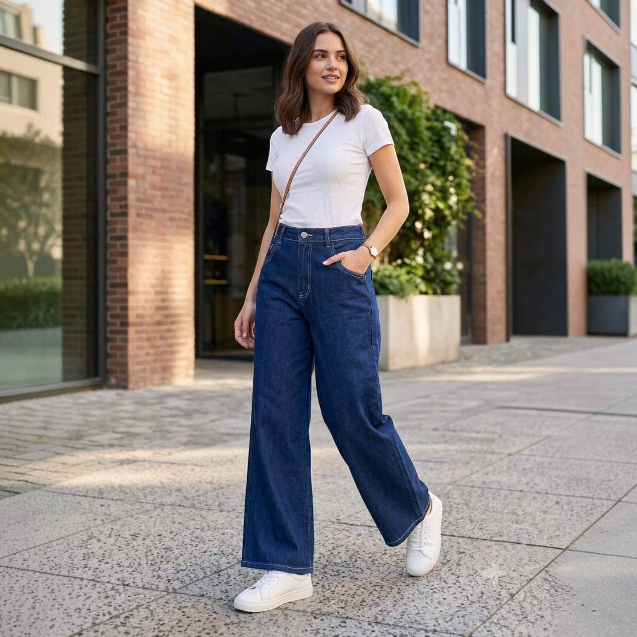 City Center high-waisted wide-leg blue jeans worn by a woman with a white t-shirt and sneakers on a city sidewalk.