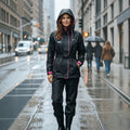 City Center woman wearing a black waterproof raincoat set with pink accents and a hood, walking on a rainy city street.