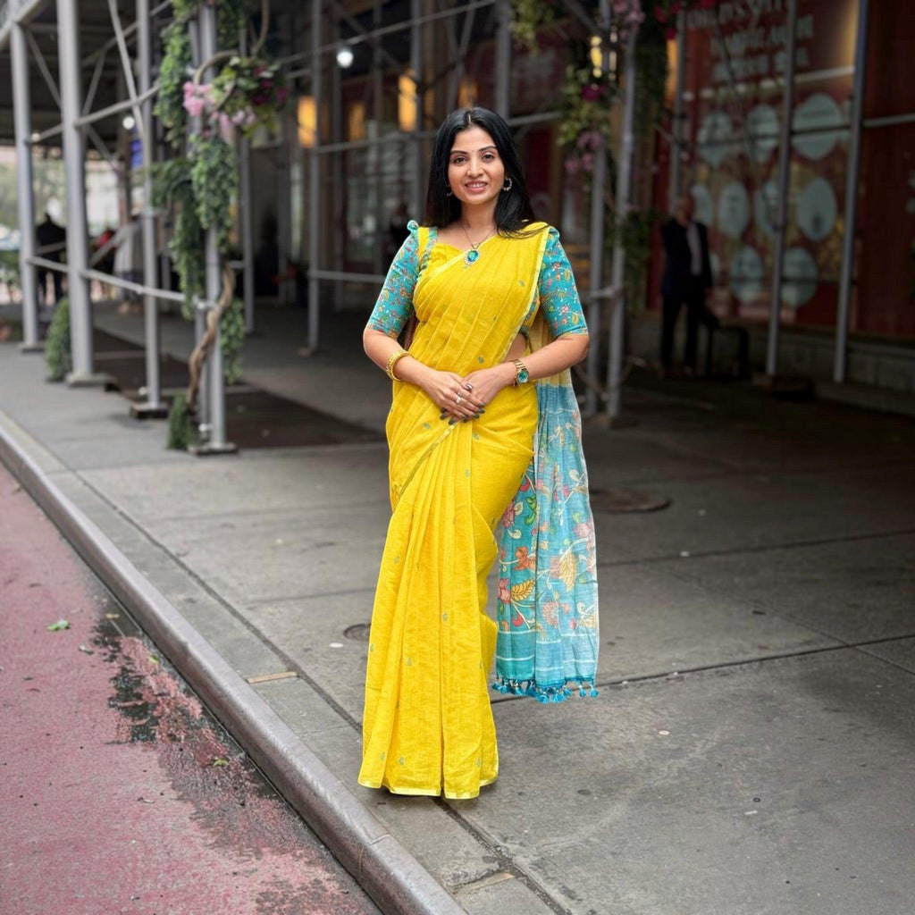 City Center premium yellow cotton saree with blue floral print blouse and pallu worn by a woman on a city sidewalk.