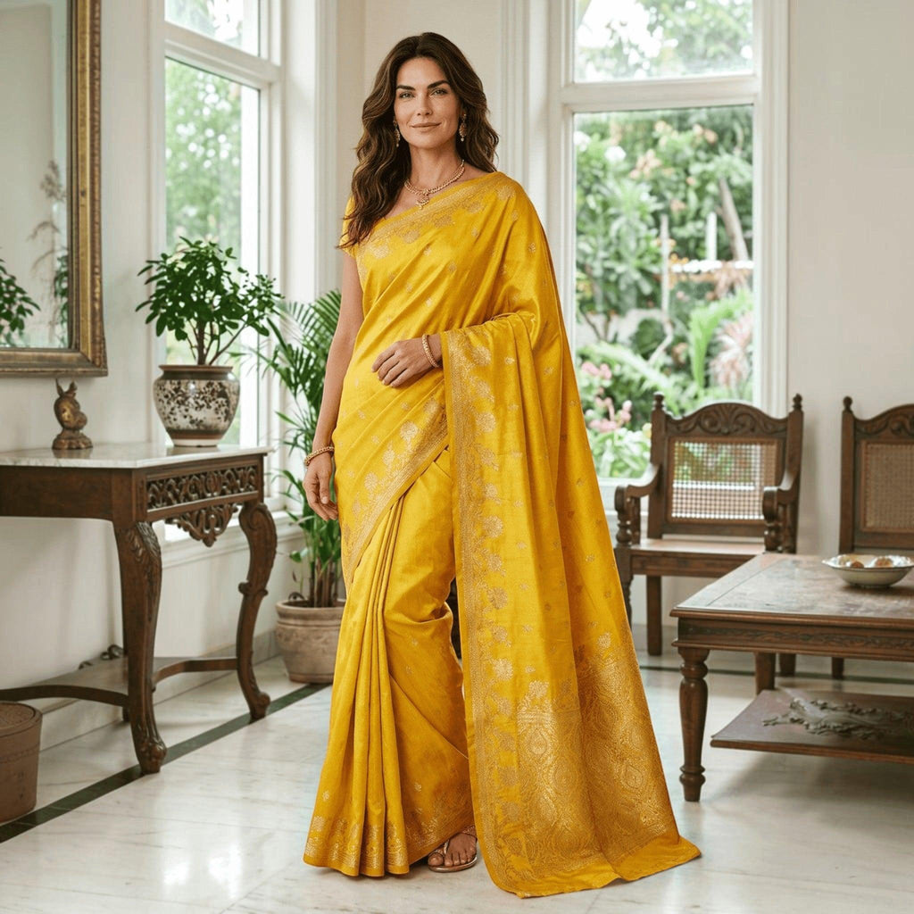 City Center yellow satin silk saree with gold floral border worn by a woman in a bright, elegant living room.