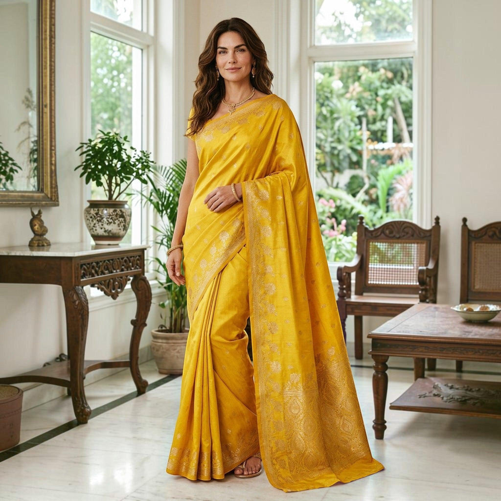 City Center yellow satin silk saree with gold floral border worn by a woman in a bright, elegant living room.